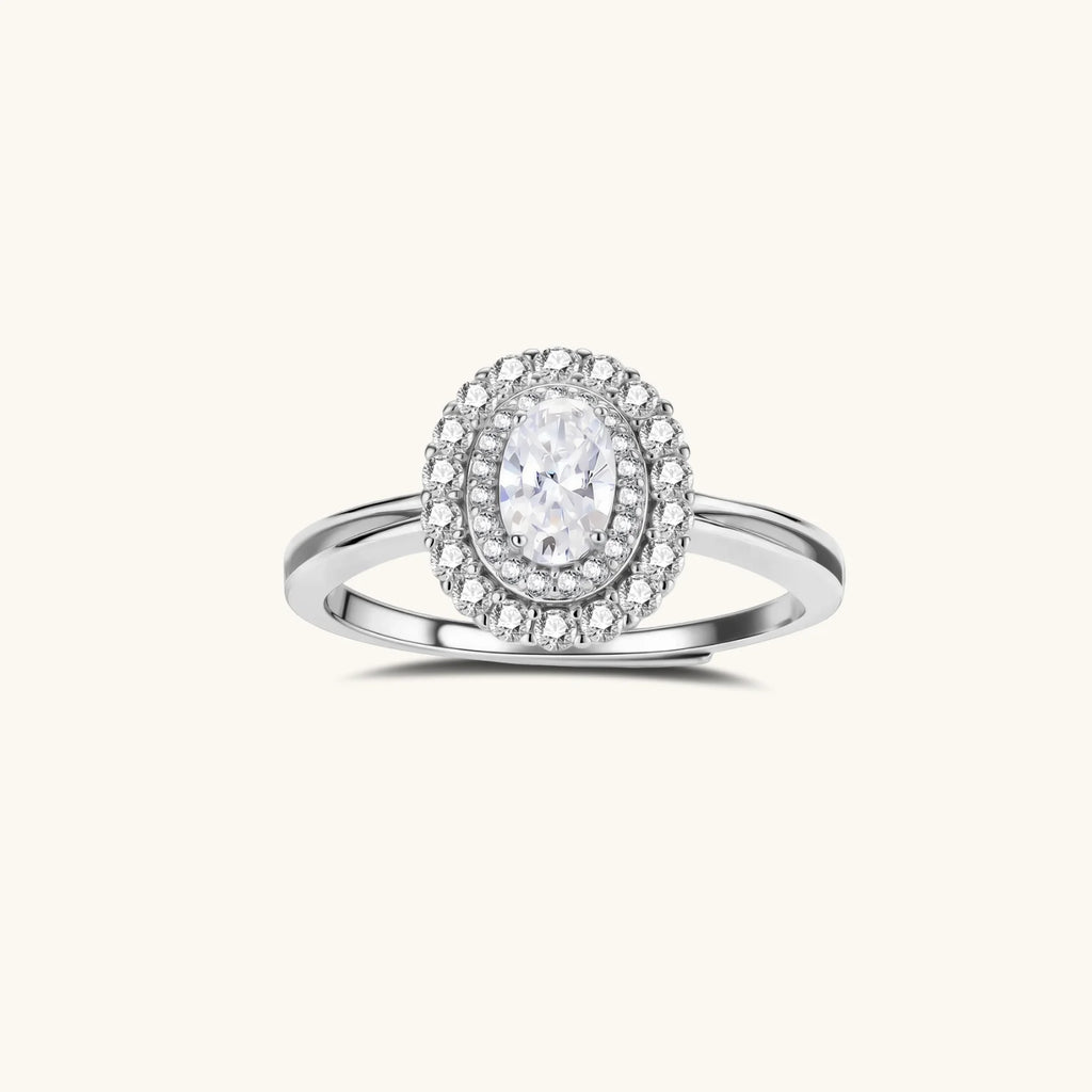 Sterling silver ring with oval moissanite center stone surrounded by double halo of sparkling stones on neutral background.