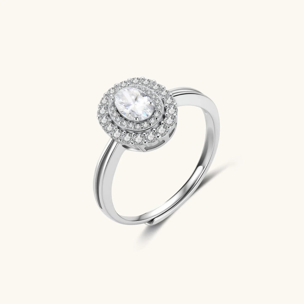 Sterling silver ring with oval moissanite center stone surrounded by double halo of sparkling stones on neutral background.