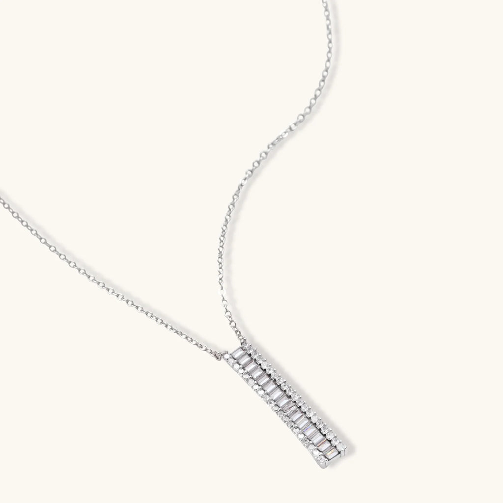 White gold plated necklace with vertical cubic zirconia pendant and matching hoop earrings on neutral background