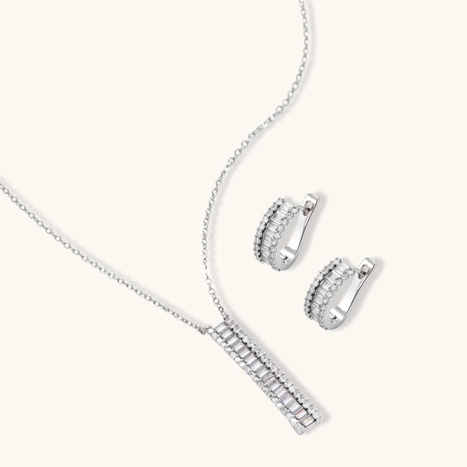 White gold plated necklace with vertical cubic zirconia pendant and matching hoop earrings on neutral background