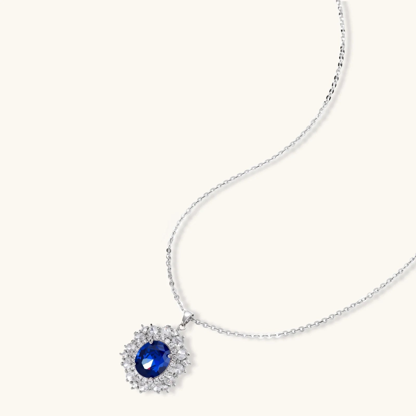 White gold plated jewelry set with blue cubic zirconia centers surrounded by clear crystal halos on cream background.