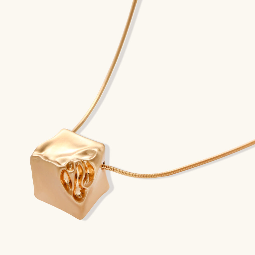 Modern cube pendant with liquid metal draping detail on adjustable chain, available in gold and silver finishes