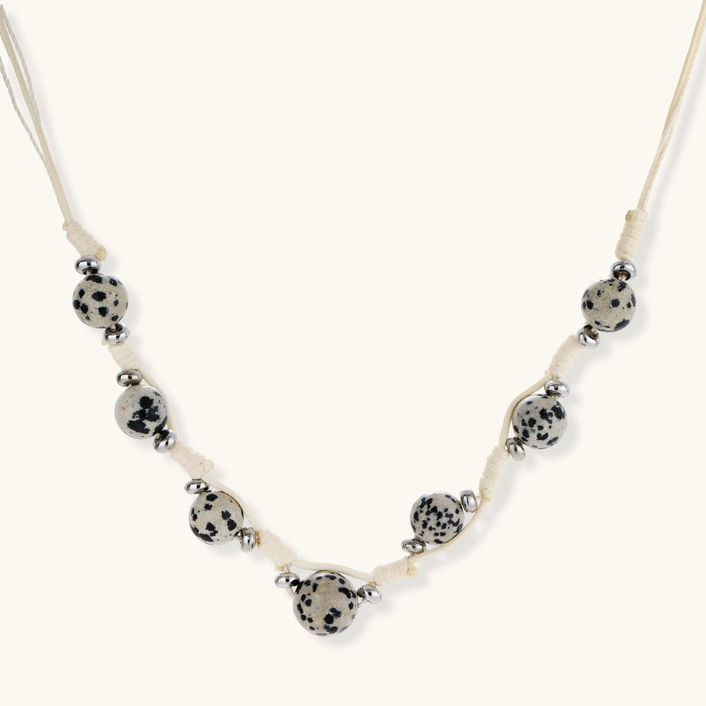 Adjustable cream cord necklace with white spotted stone beads featuring black speckles on neutral background