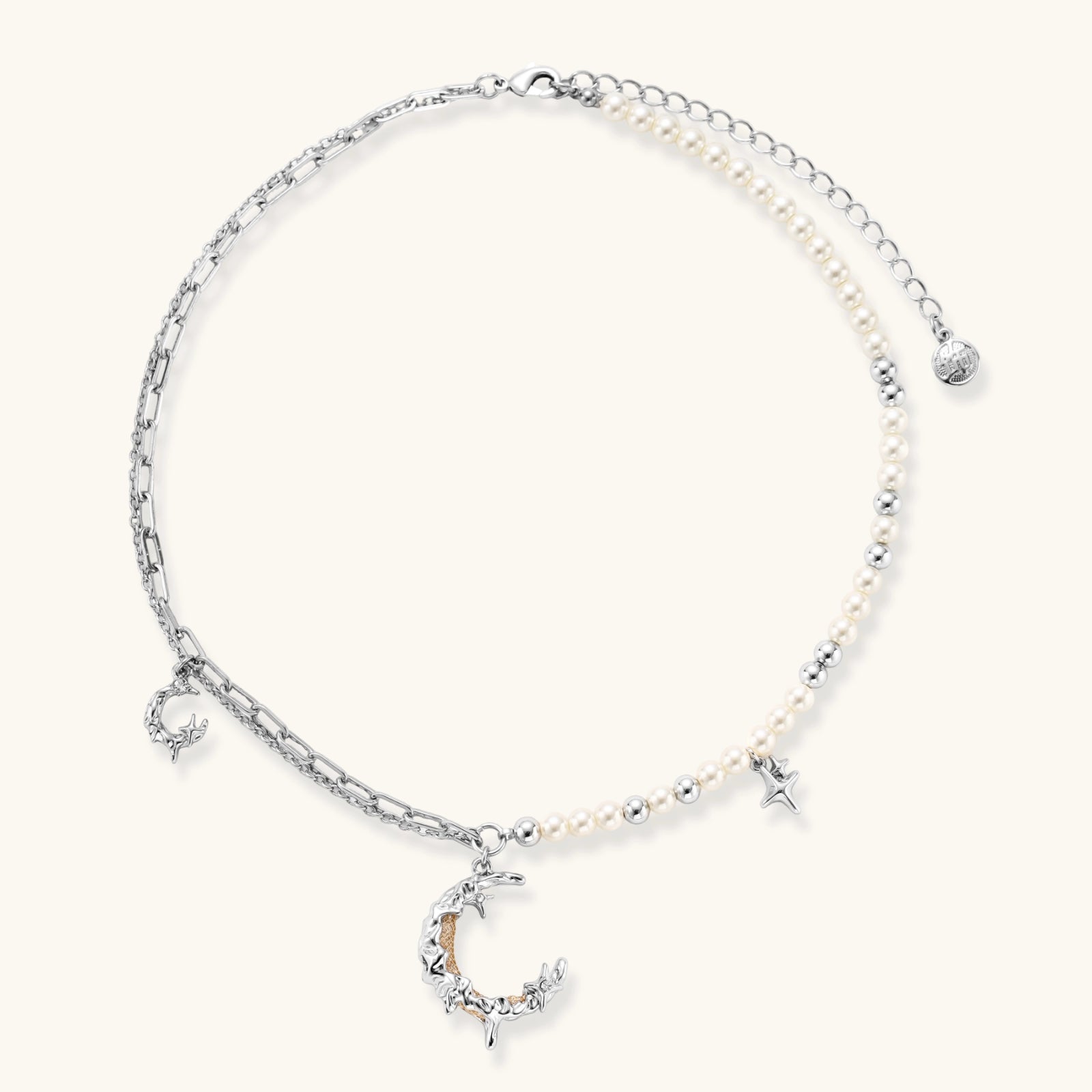 Silver-toned crescent moon pendant with star accents on pearl and chain necklace against white background.