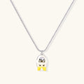 Chrome egg-shaped pendant with kawaii face, yellow bow, and pearl detail on silver chain against white background