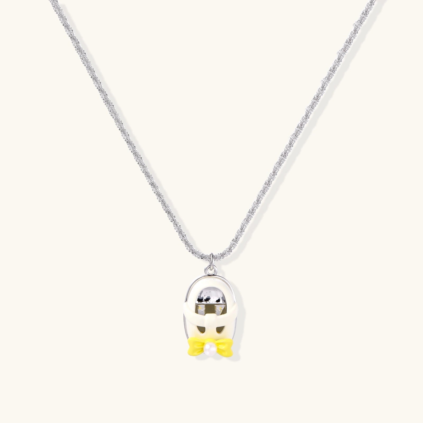 Chrome egg-shaped pendant with kawaii face, yellow bow, and pearl detail on silver chain against white background