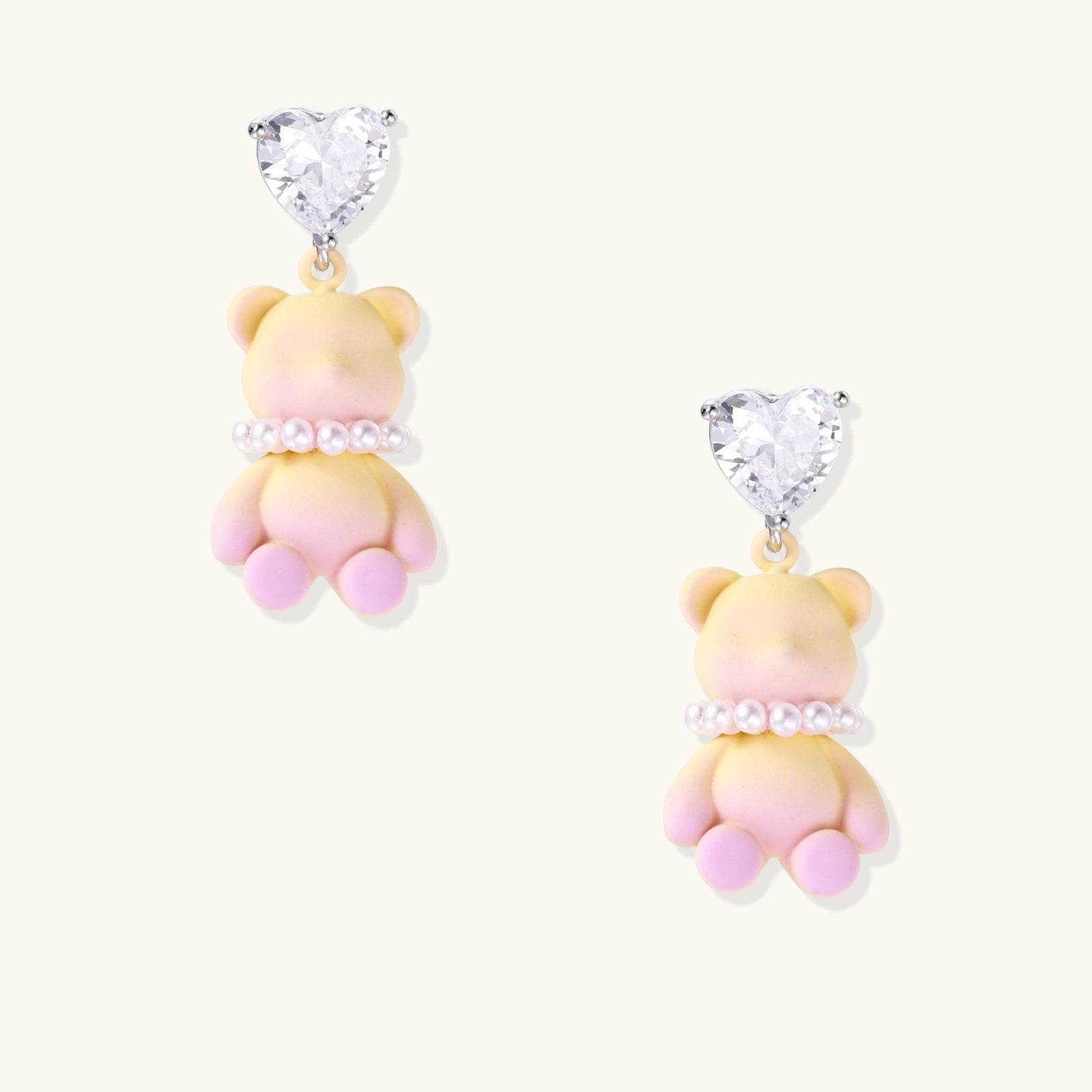 Pastel gradient teddy bear drop earrings with clear heart studs and pearl details on white background.