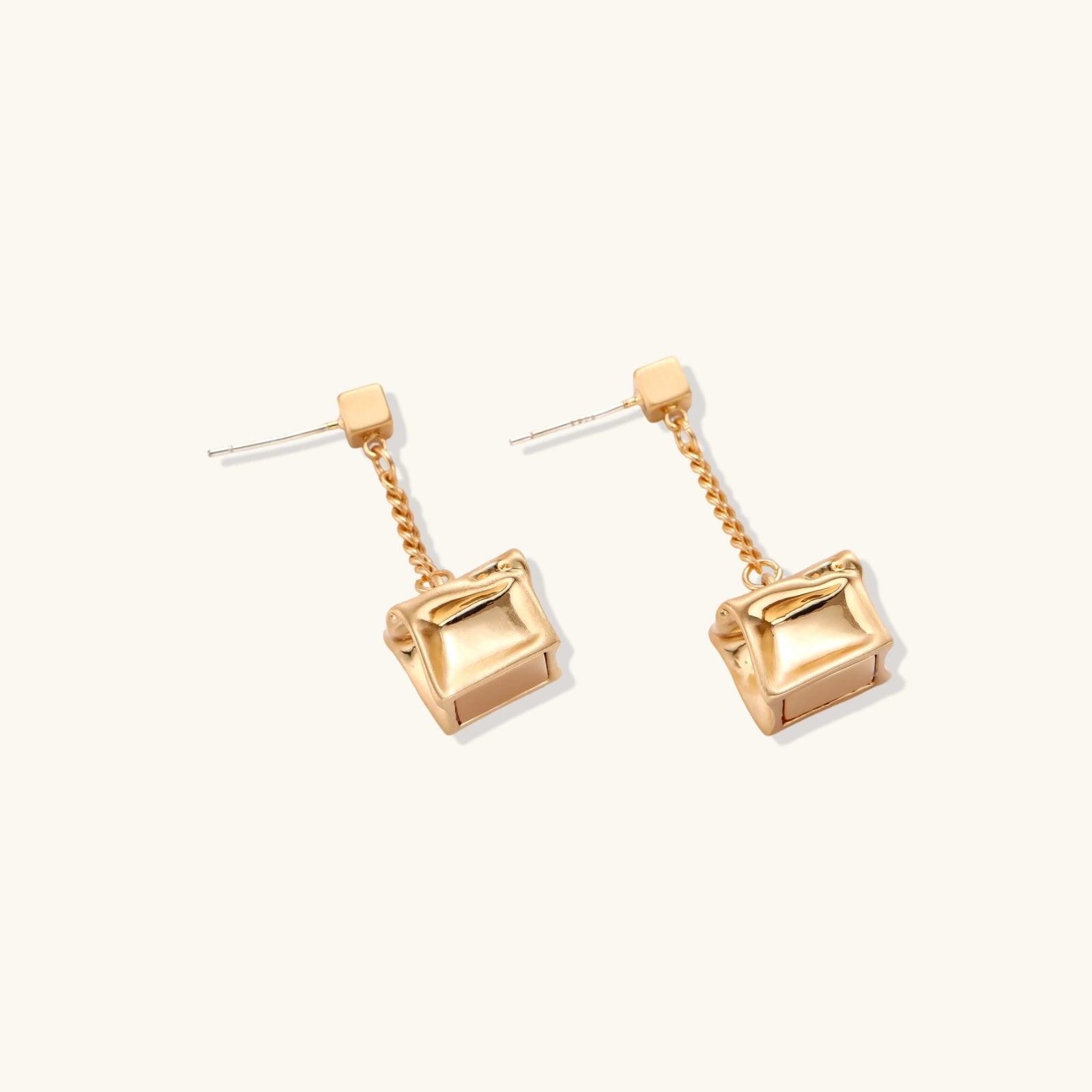 Modern geometric jewelry set featuring crumpled cube pendants in warm gold finish with chain details on beige background.