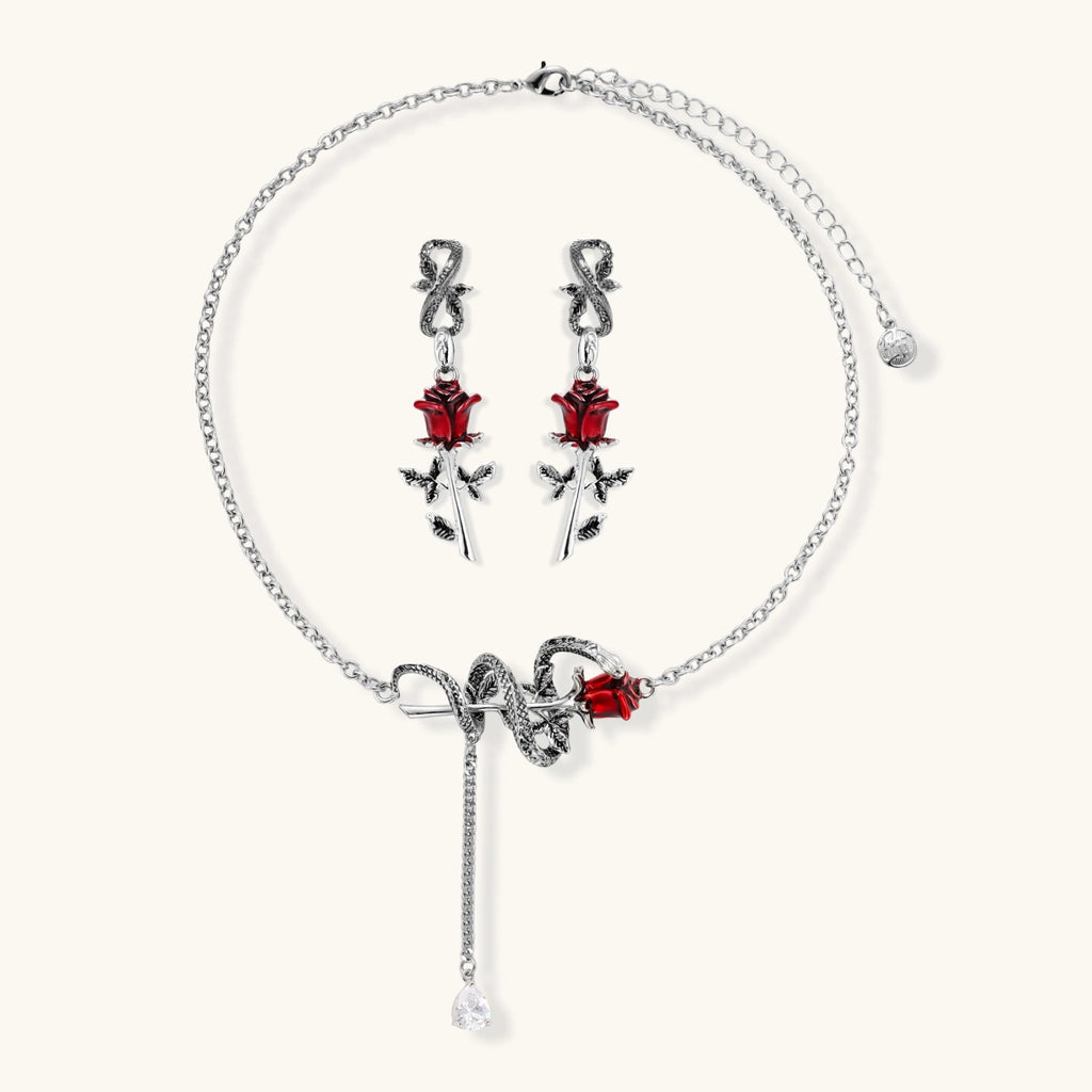 Gothic jewelry set with silver snake designs holding red enamel roses, featuring detailed leaf stems on cream background