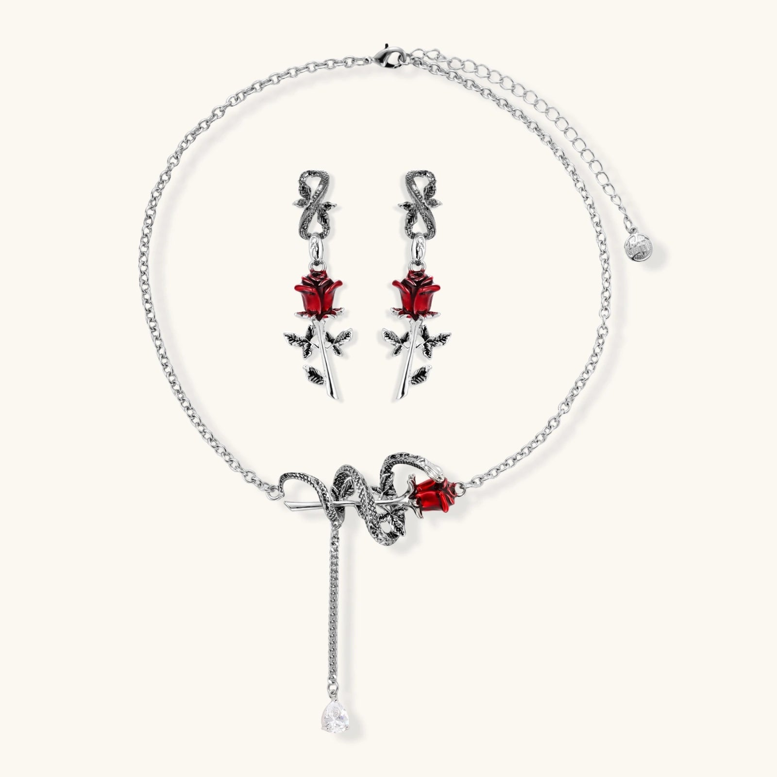 Gothic jewelry set with silver snake designs holding red enamel roses, featuring detailed leaf stems on cream background