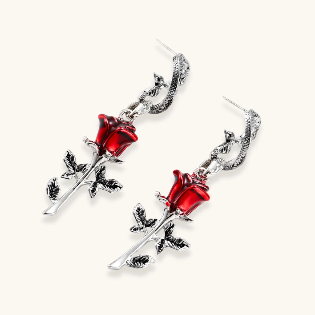 Gothic jewelry set with silver snake designs holding red enamel roses, featuring detailed leaf stems on cream background