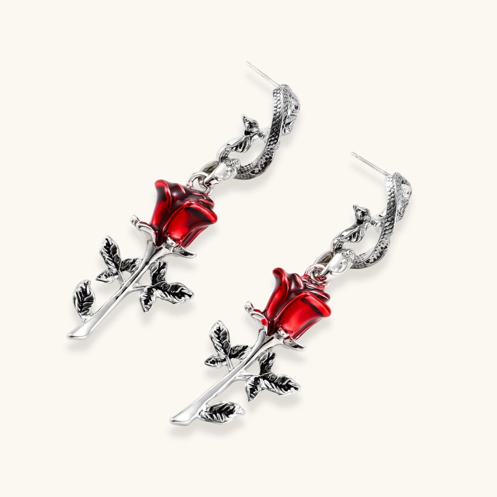 Gothic jewelry set with silver snake designs holding red enamel roses, featuring detailed leaf stems on cream background