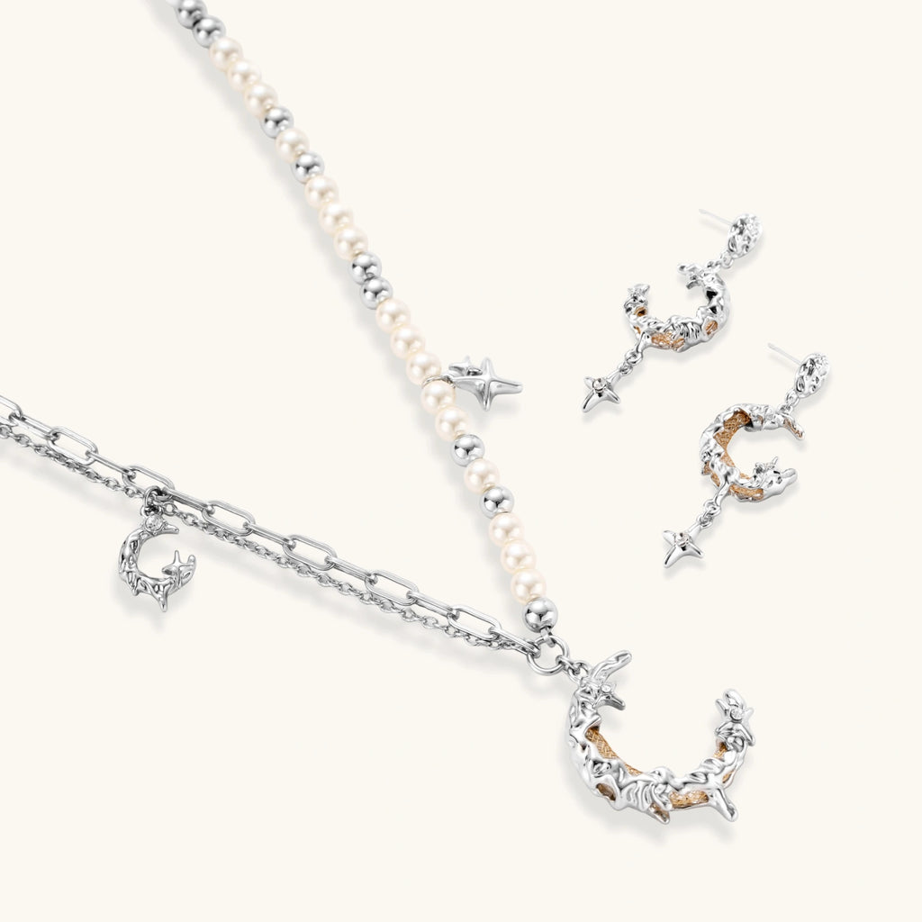 Mixed-metal jewelry set featuring layered necklaces with crescent moon pendant and pearl beads, plus matching star-drop earrings.