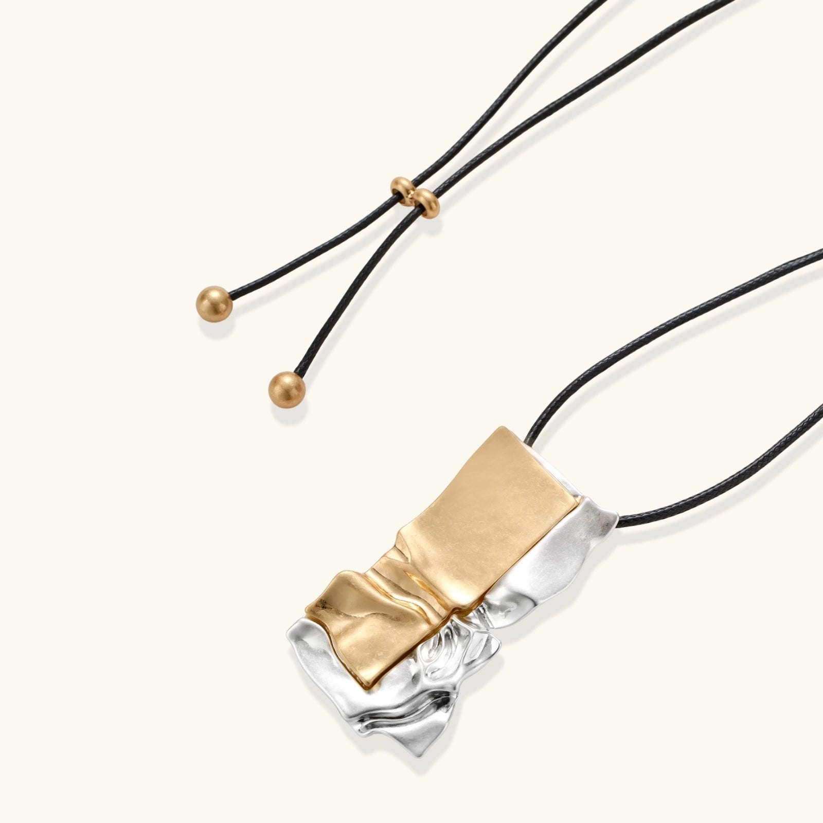 Abstract sculptural pendant necklace with gold and silver toned eco-zinc alloy on black adjustable cord with brass bead details