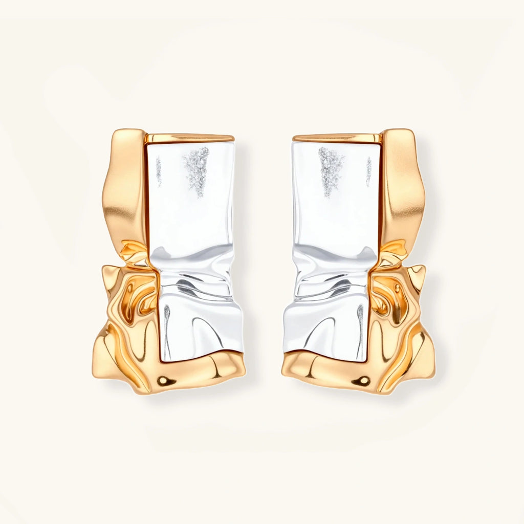 Close-up of avant-garde sculptural earrings with flowing liquid metal design in gold and silver tones on white background.
