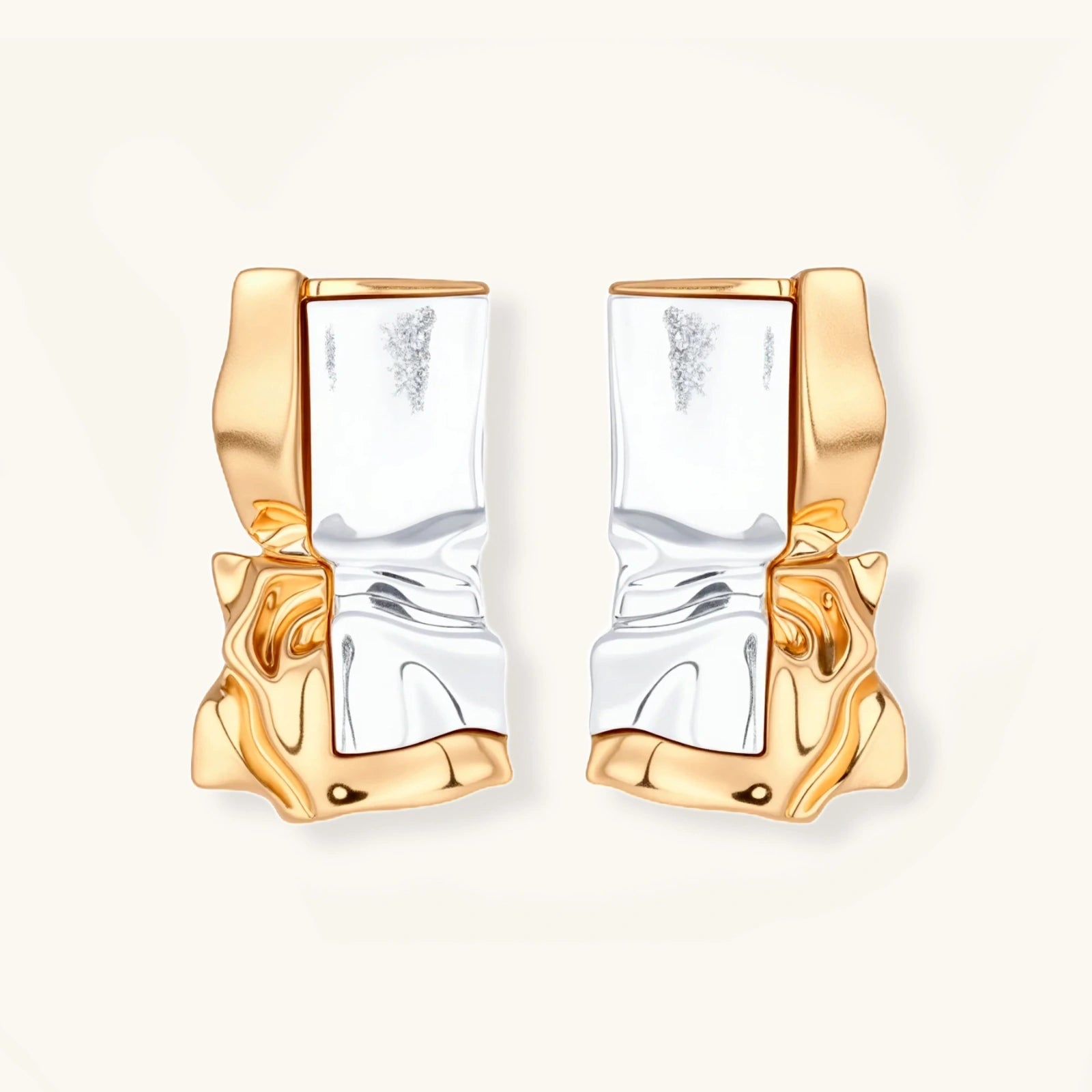Close-up of avant-garde sculptural earrings with flowing liquid metal design in gold and silver tones on white background.