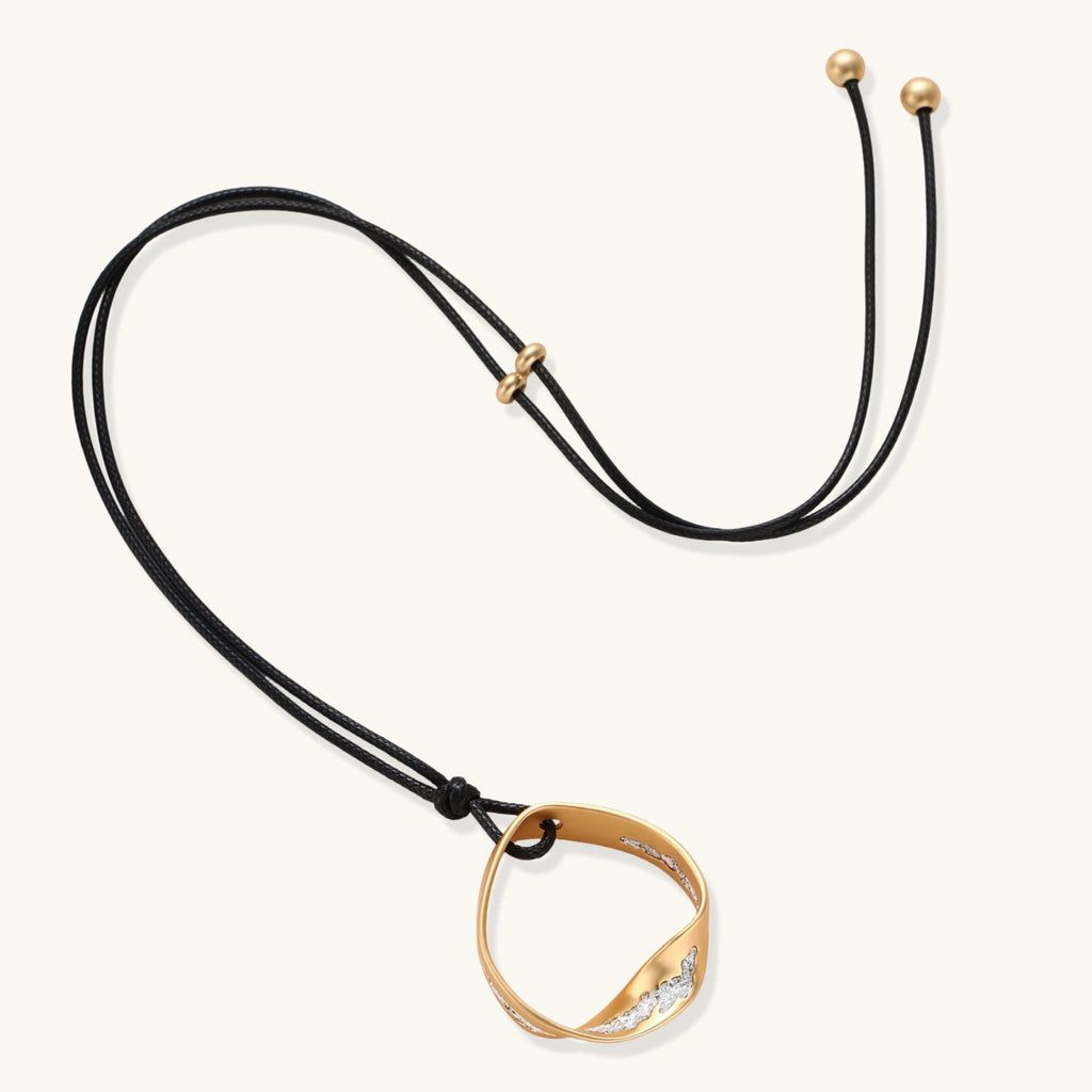 Geometric circle pendant necklace with crystal cluster on adjustable black cord, available in gold and silver finishes.