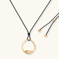 Geometric circle pendant necklace with crystal cluster on adjustable black cord, available in gold and silver finishes.