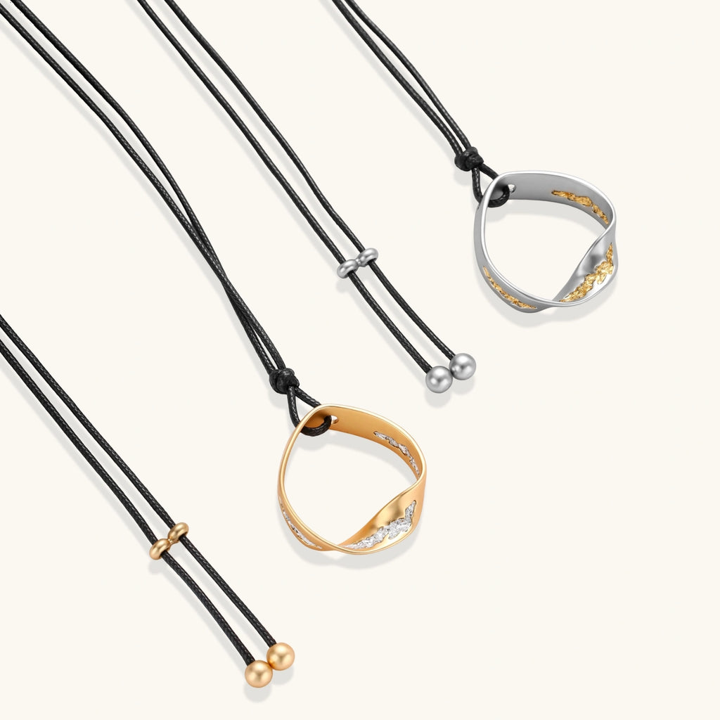 Adjustable black cord necklace with circular gold pendant featuring sparkly crystal accents on white background.