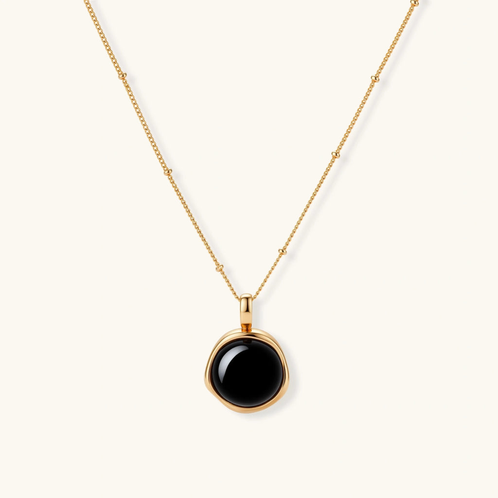 Circular black agate pendant on gold-plated sterling silver chain against cream background, showing modern minimalist design.