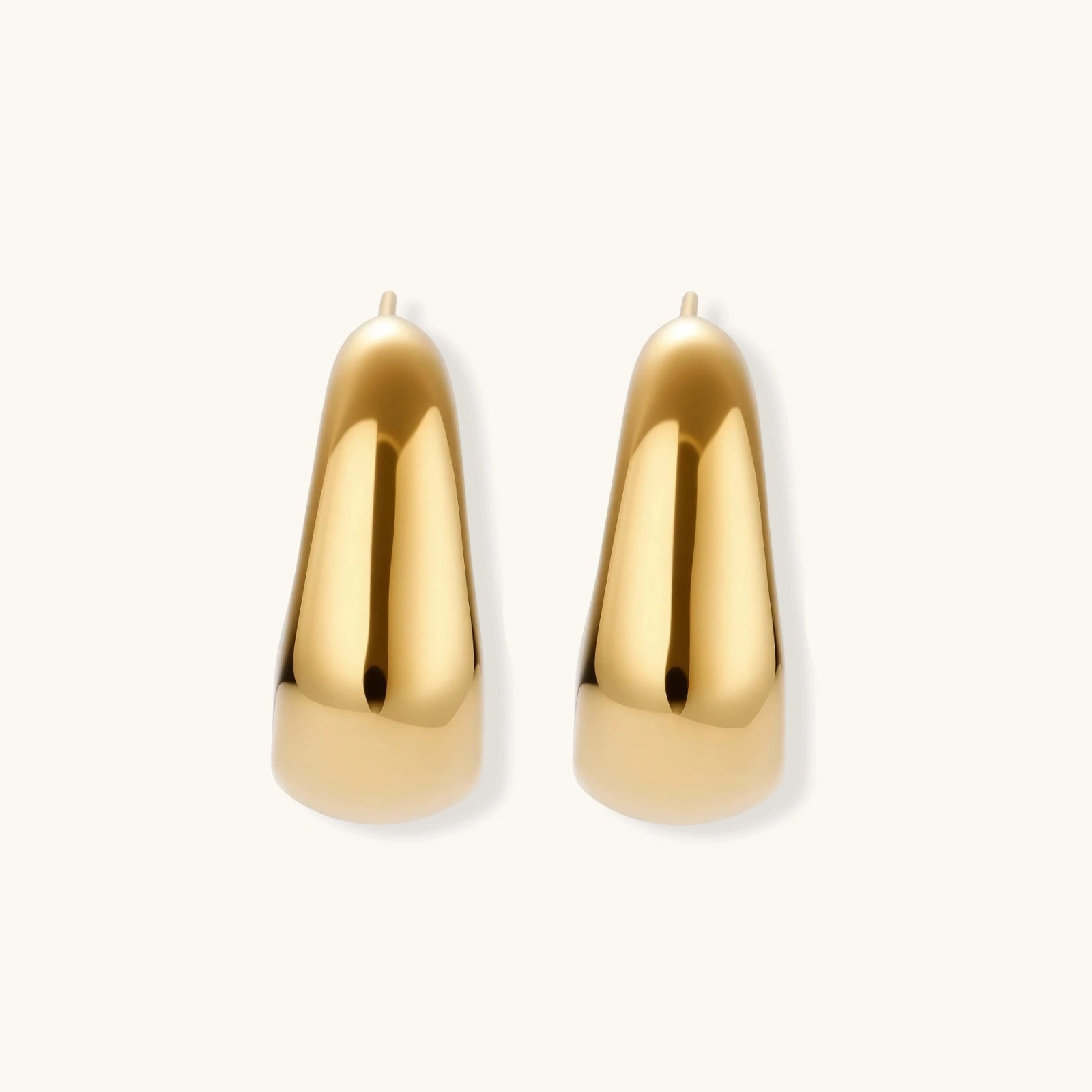 Close-up of curved gold-plated huggie earrings with sculptural design on white background, showing polished finish.