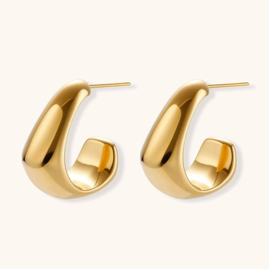 Close-up of curved gold-plated huggie earrings with sculptural design on white background, showing polished finish.