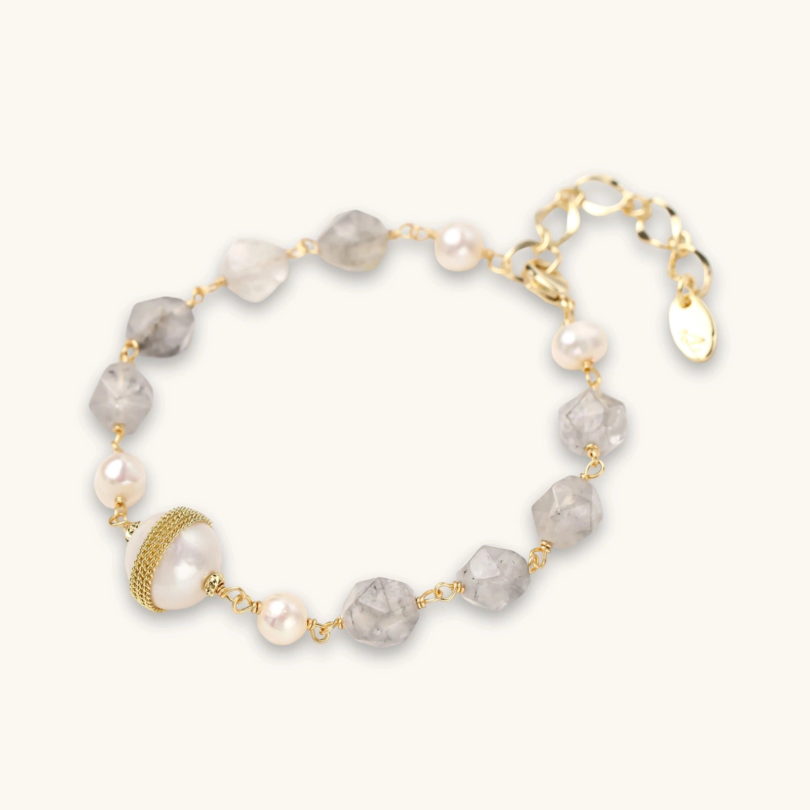 Bracelet with cloudy quartz beads, freshwater pearls, and gold-wrapped baroque pearl centerpiece on white background.