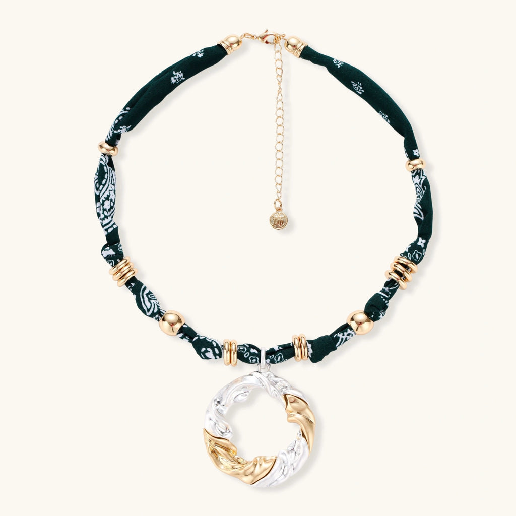 Adjustable necklace with black paisley fabric cord, gold metal spacers, and clear twisted pendant on cream background