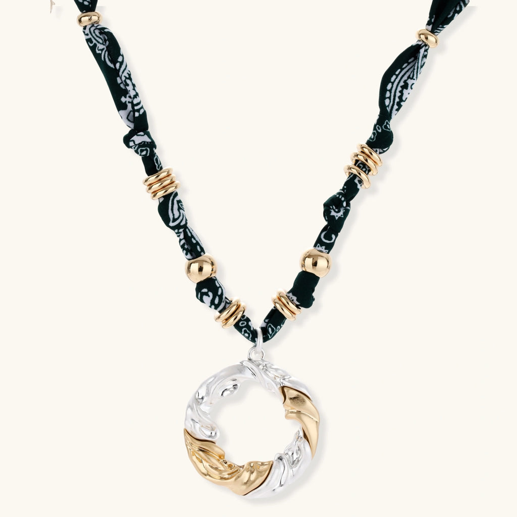 Adjustable necklace with black paisley fabric cord, gold metal spacers, and clear twisted pendant on cream background