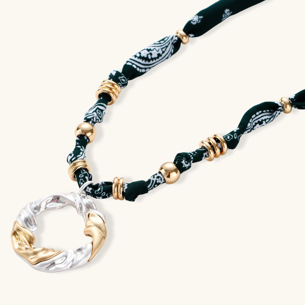 Adjustable necklace with black paisley fabric cord, gold metal spacers, and clear twisted pendant on cream background