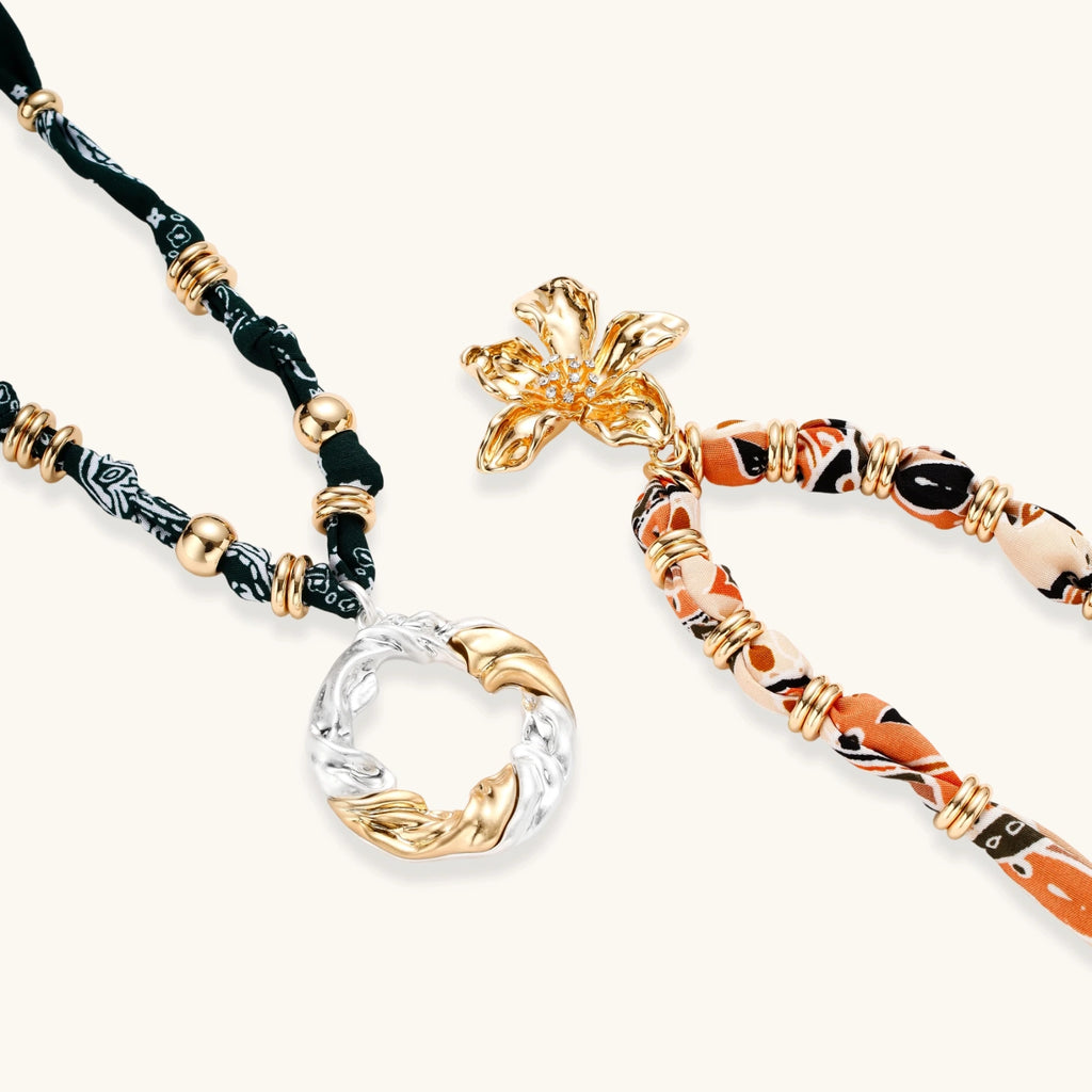 Adjustable necklace with black paisley fabric cord, gold metal spacers, and clear twisted pendant on cream background