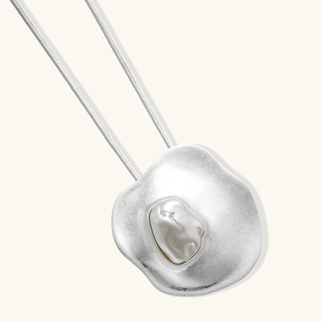 Sculptural silver necklace with flowing organic pendant featuring centered baroque pearl on white background.