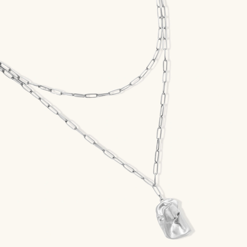 Silver layered necklace with organic flowing pendant in eco-zinc alloy on neutral background, showing adjustable chain design.