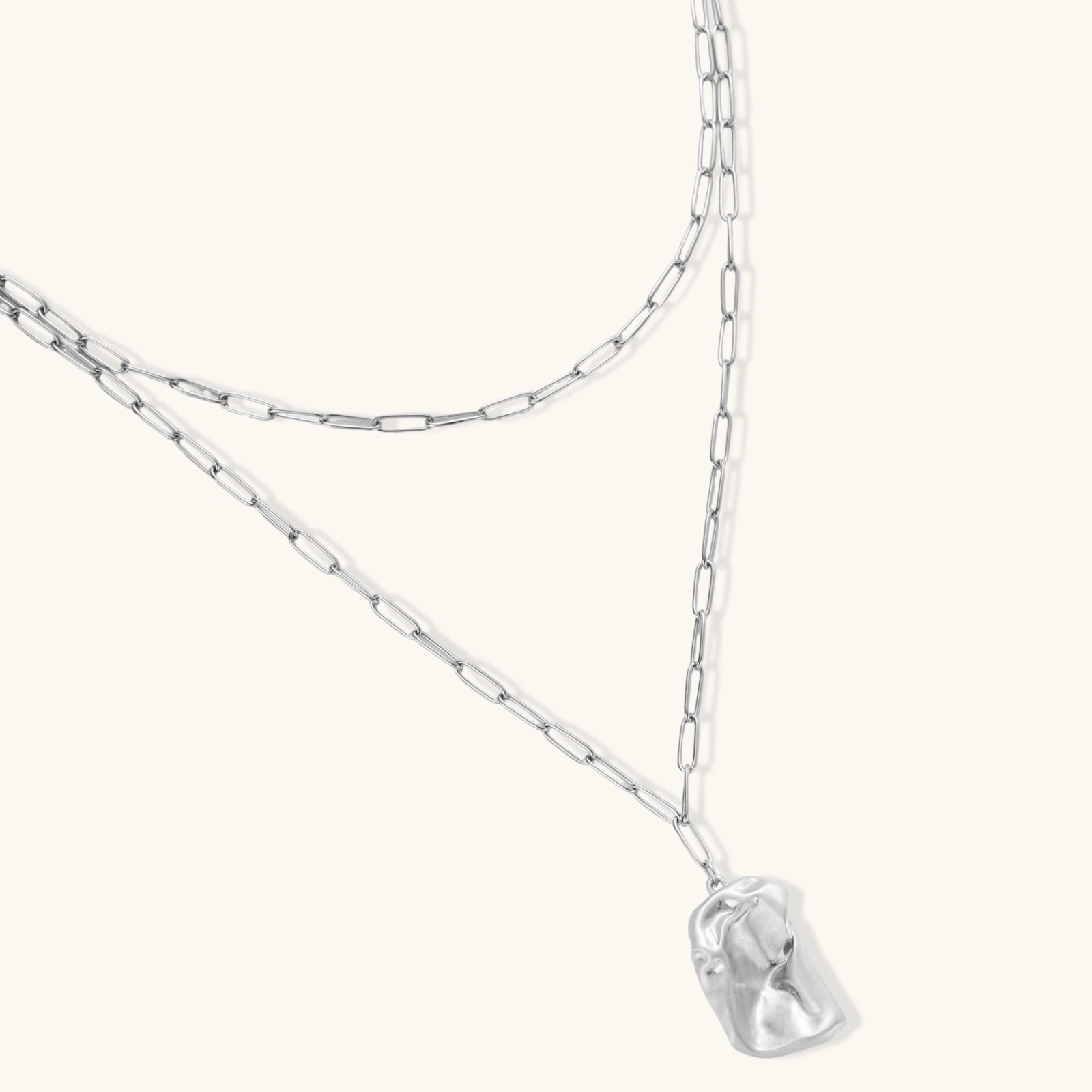 Silver layered necklace with organic flowing pendant in eco-zinc alloy on neutral background, showing adjustable chain design.