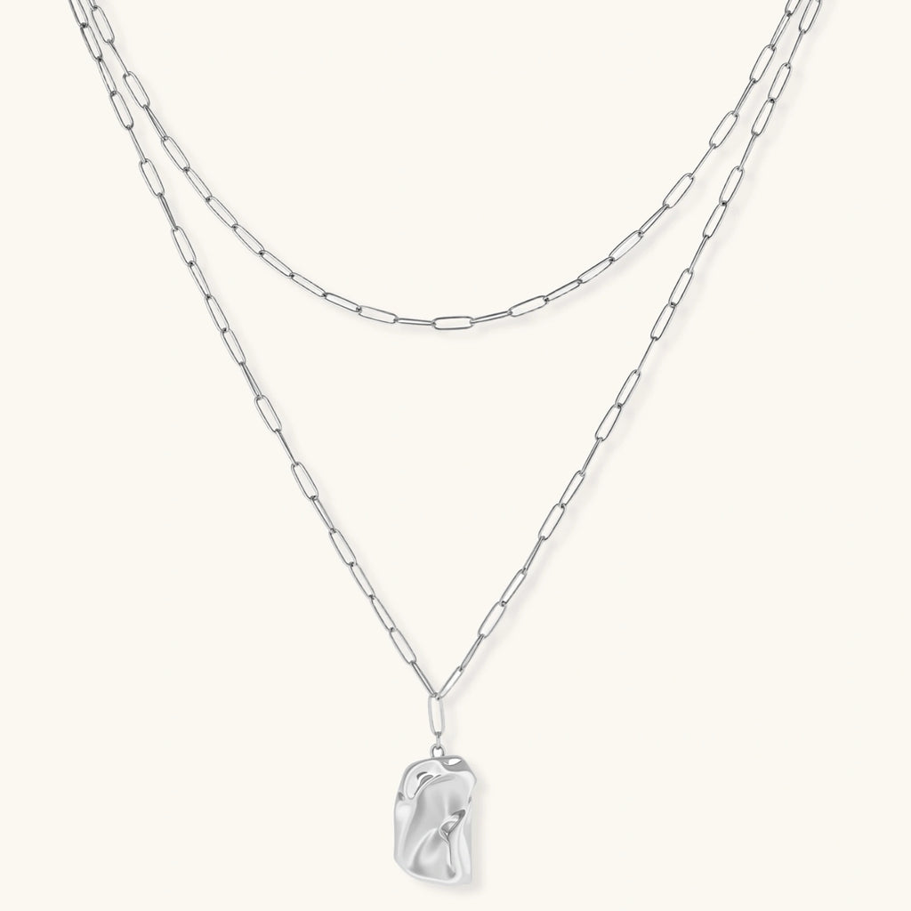 Silver layered necklace with organic flowing pendant in eco-zinc alloy on neutral background, showing adjustable chain design.