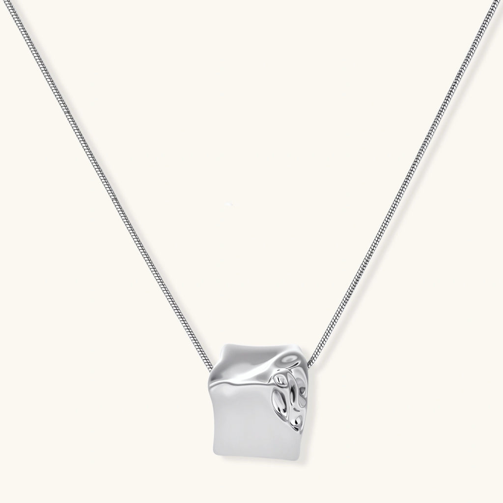 Close-up of a silver-toned molten cube pendant necklace with organic flowing texture on a minimalist chain