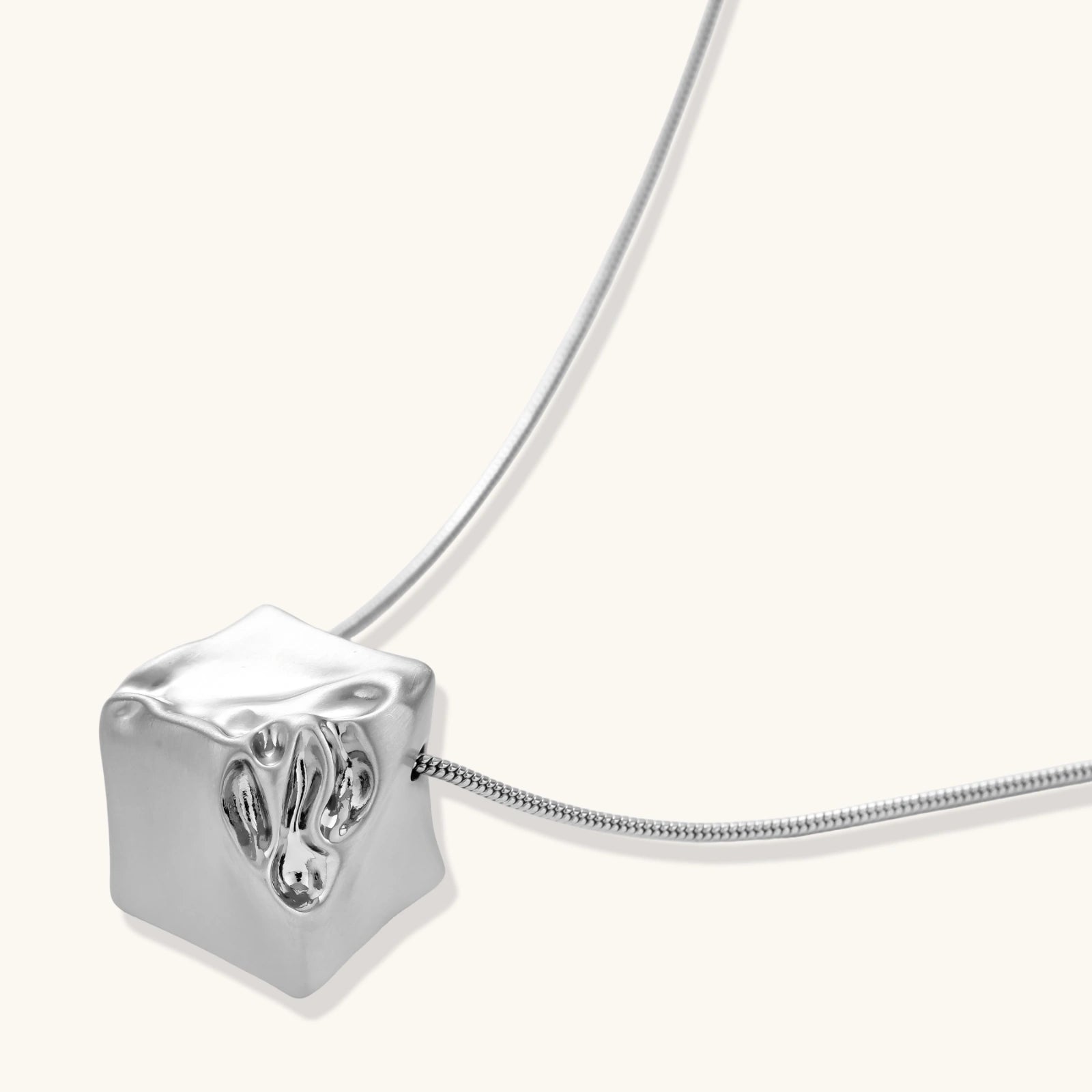 Close-up of a silver-toned molten cube pendant necklace with organic flowing texture on a minimalist chain
