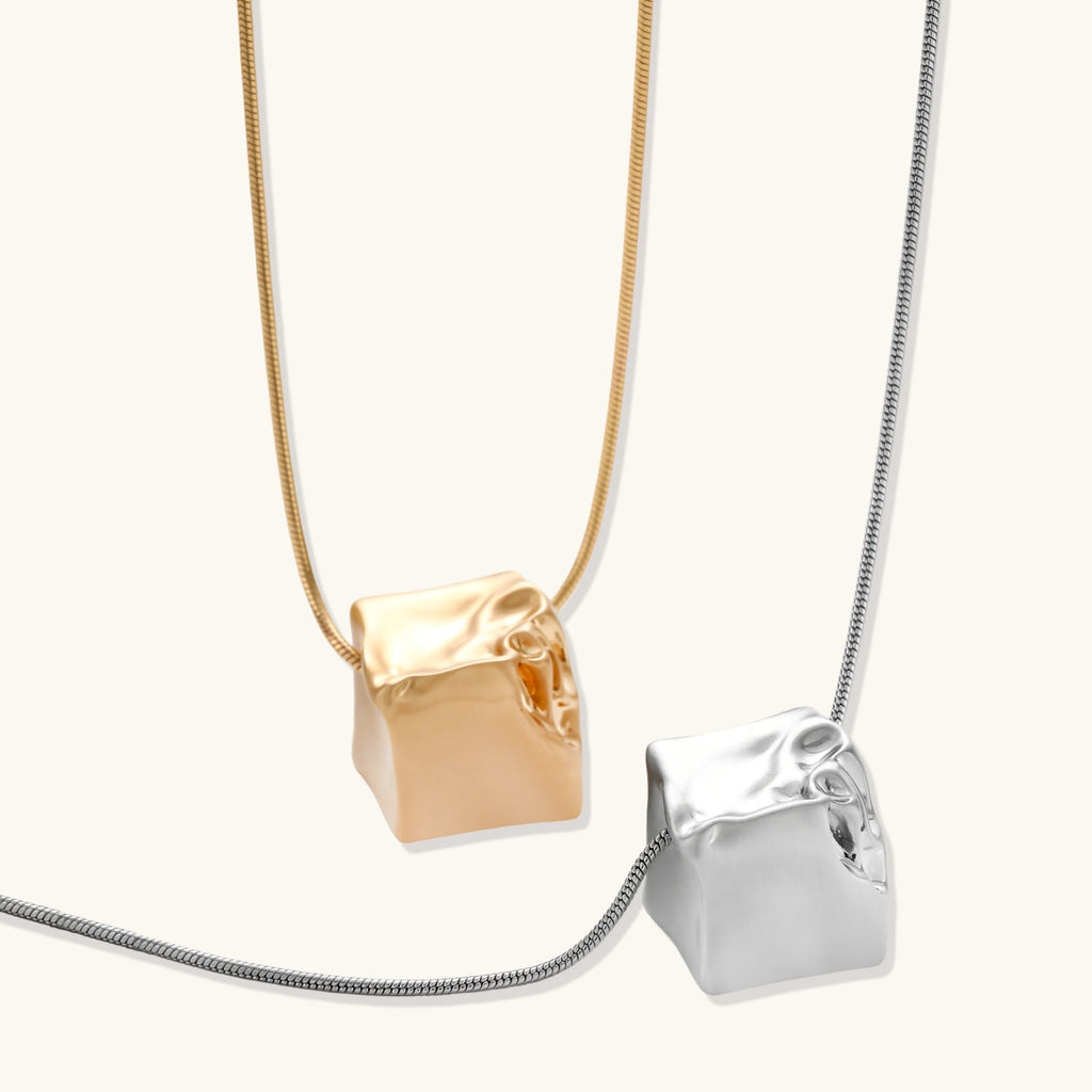 Close-up of a silver-toned molten cube pendant necklace with organic flowing texture on a minimalist chain