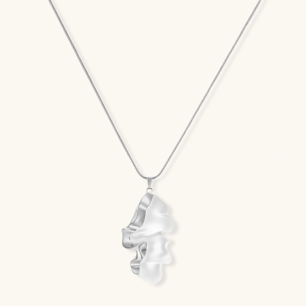 Modern sculptural pendant necklace with twisted metallic design on delicate silver chain against neutral background.