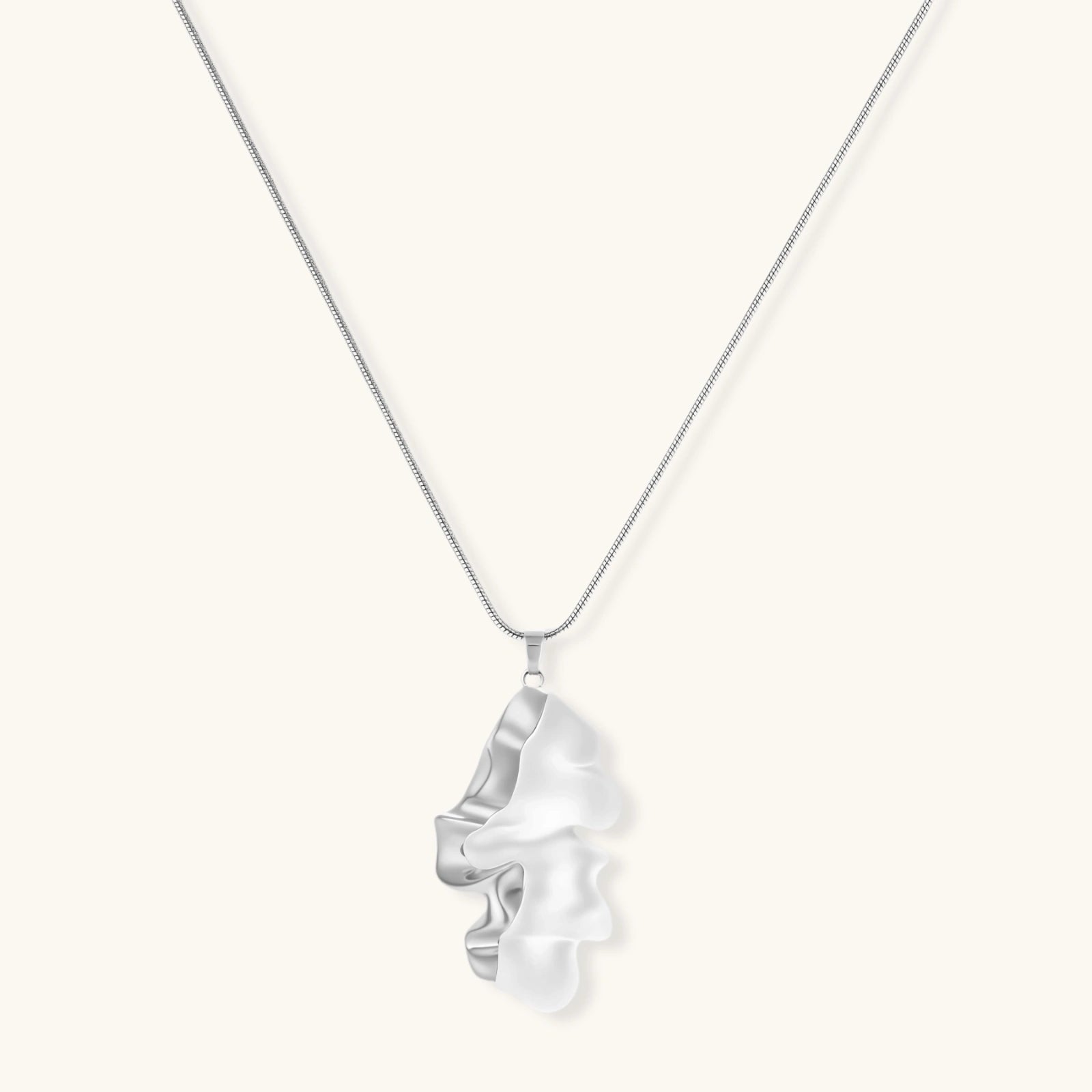 Modern sculptural pendant necklace with twisted metallic design on delicate silver chain against neutral background.