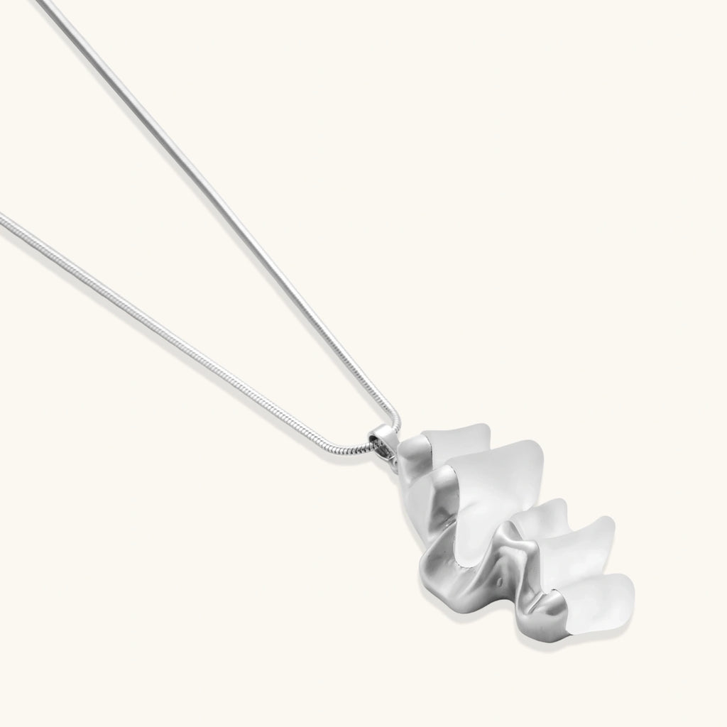 Modern sculptural pendant necklace with twisted metallic design on delicate silver chain against neutral background.