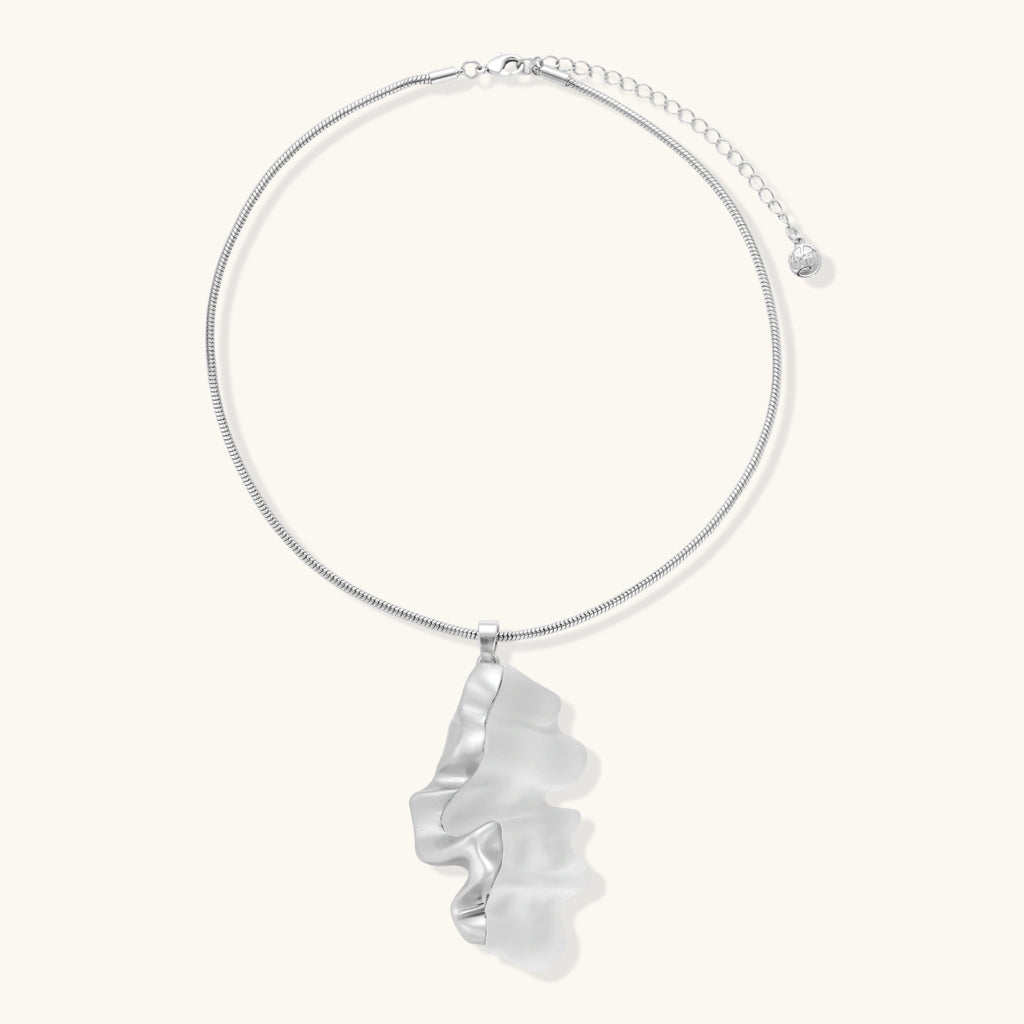 Modern sculptural pendant necklace with twisted metallic design on delicate silver chain against neutral background.