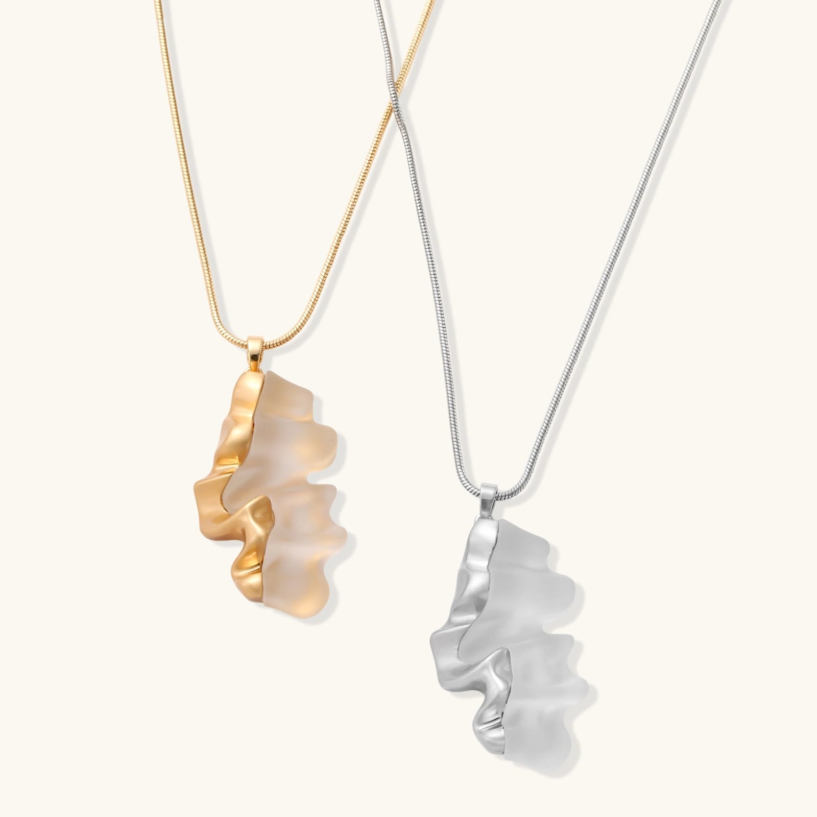 Modern sculptural pendant necklace with twisted metallic design on delicate silver chain against neutral background.