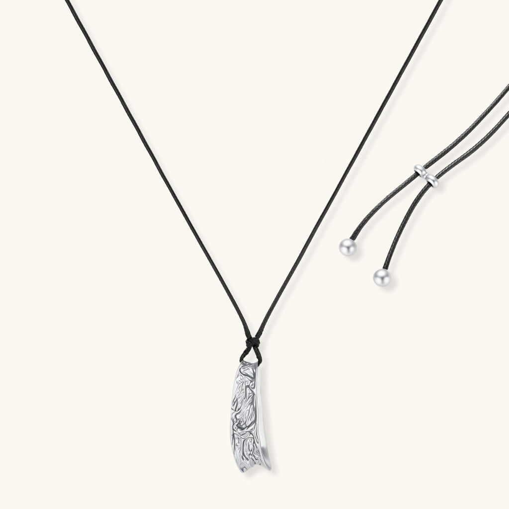 Adjustable black cord necklace with intricate silver-toned pendant featuring ornamental relief patterns and bead details.