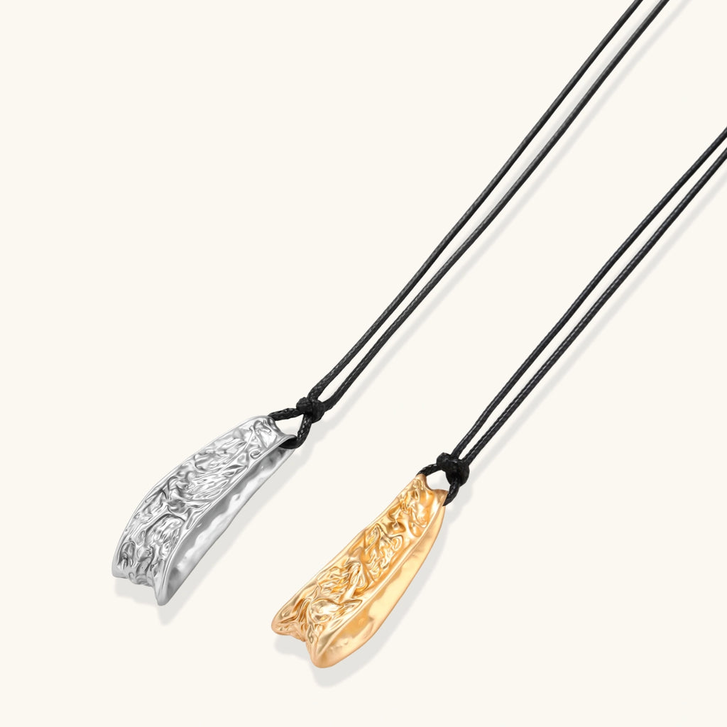 Adjustable black cord necklace with intricate silver-toned pendant featuring ornamental relief patterns and bead details.