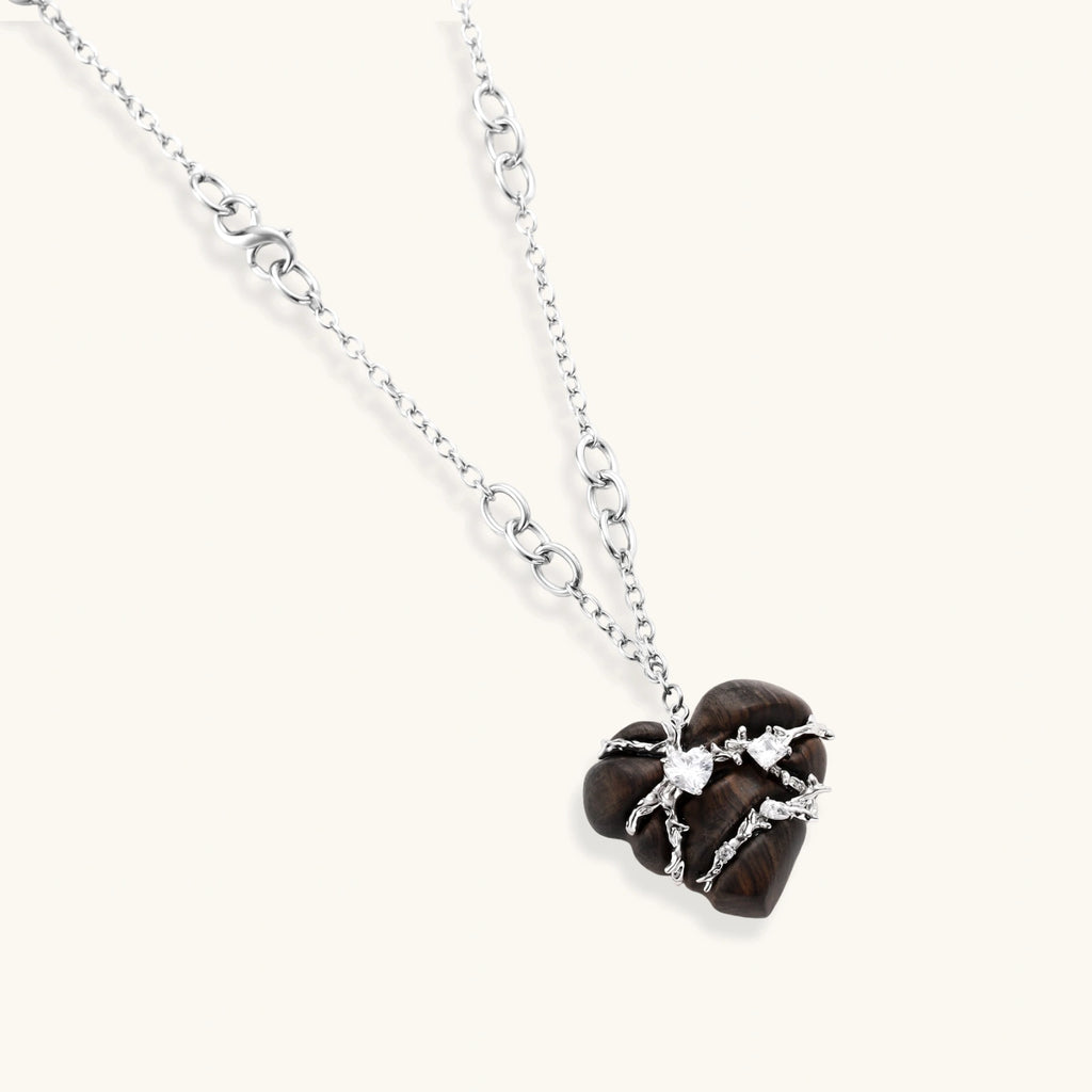 Dark ebony wood heart pendant wrapped with brass wire and zirconia crystals on adjustable chain against cream background