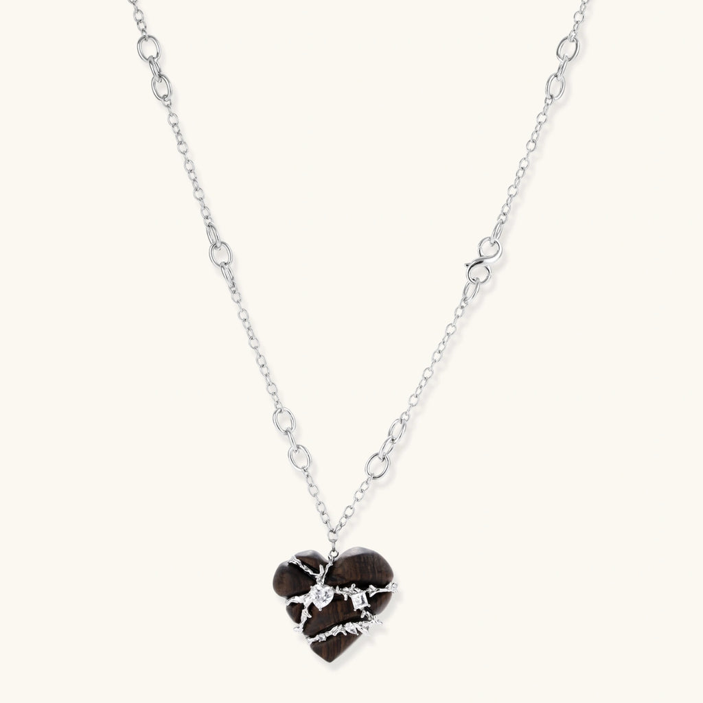 Dark ebony wood heart pendant wrapped with brass wire and zirconia crystals on adjustable chain against cream background