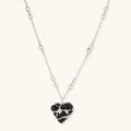 Dark ebony wood heart pendant wrapped with brass wire and zirconia crystals on adjustable chain against cream background