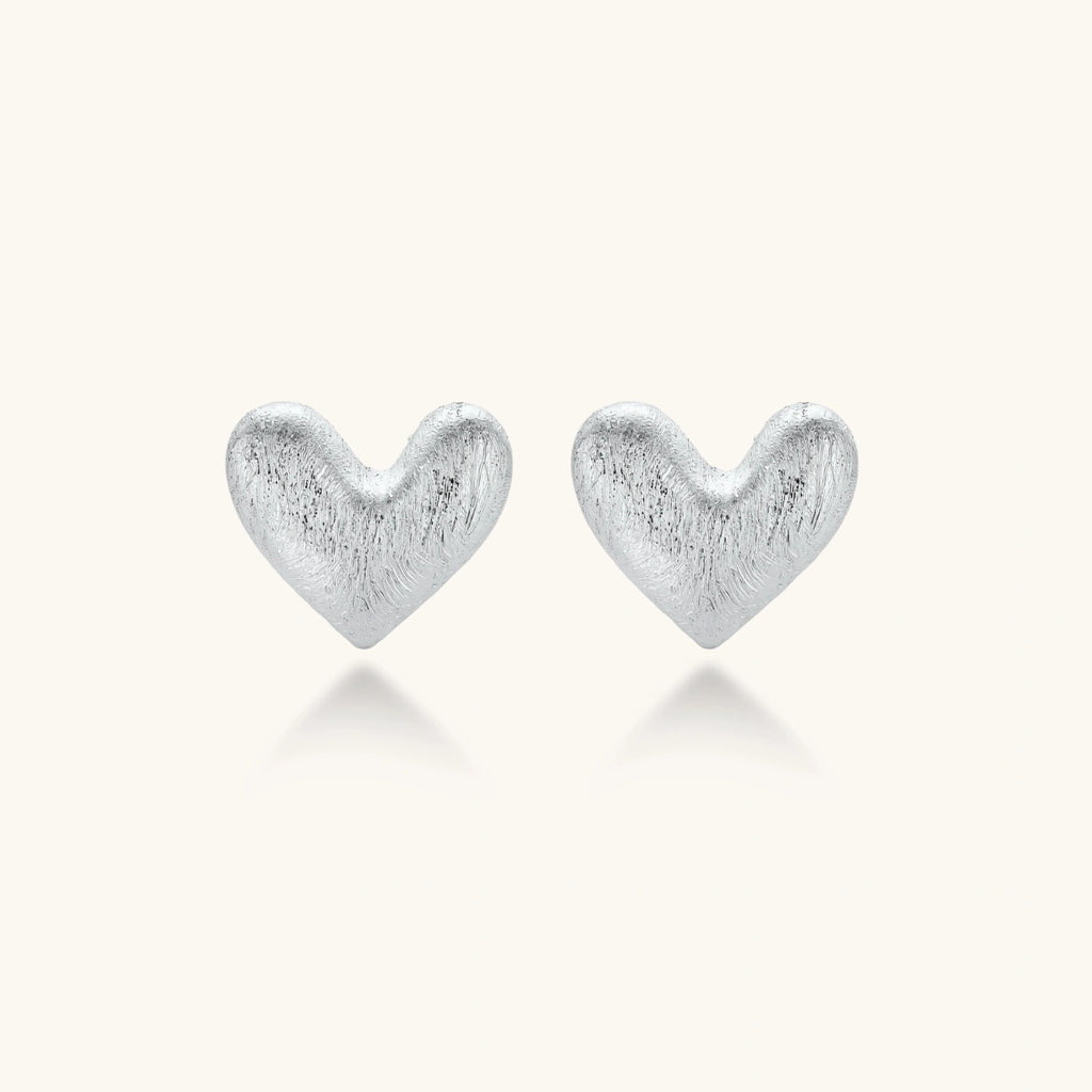 Pair of brushed platinum-plated 925 sterling silver puffy heart stud earrings on a cream background.