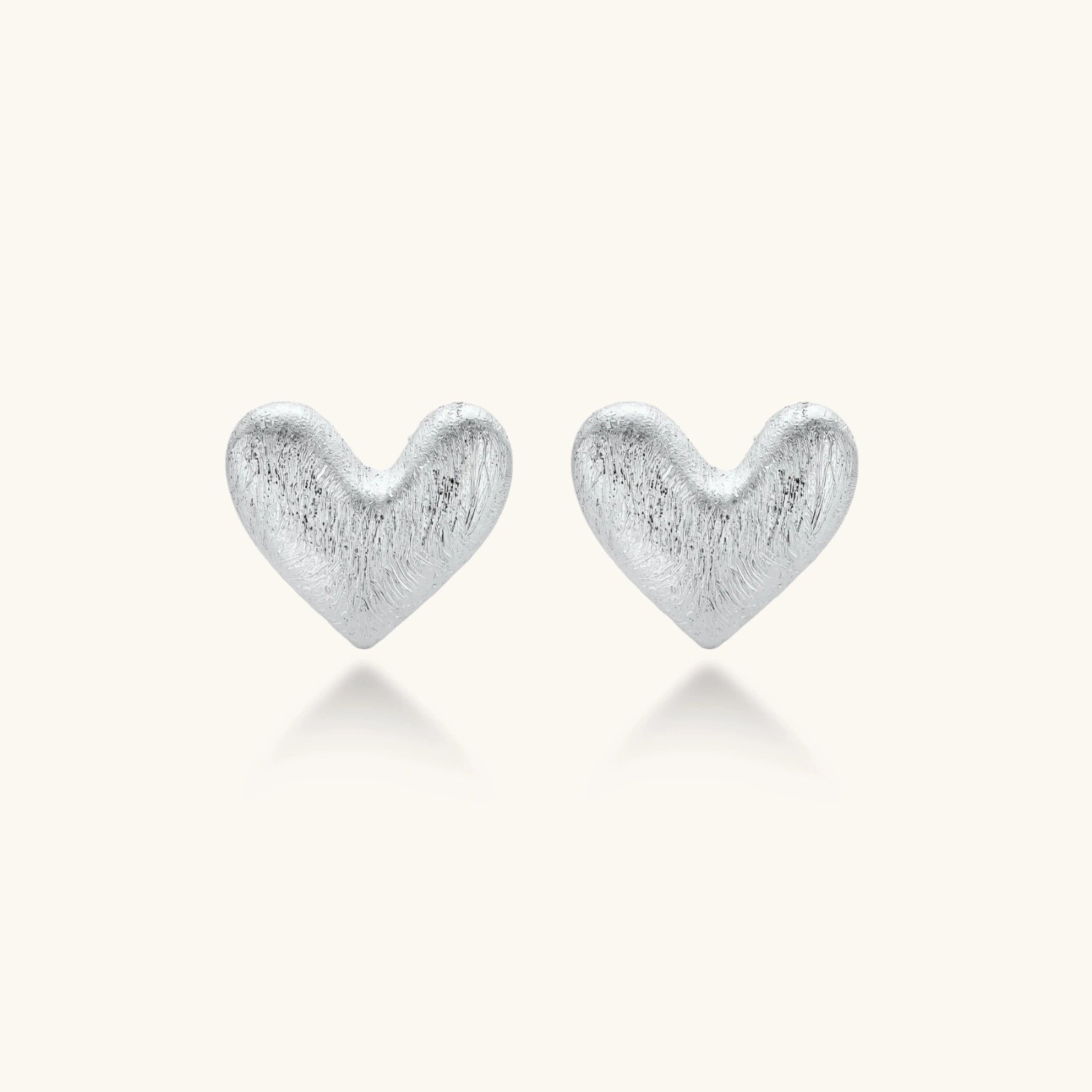 Pair of brushed platinum-plated 925 sterling silver puffy heart stud earrings on a cream background.